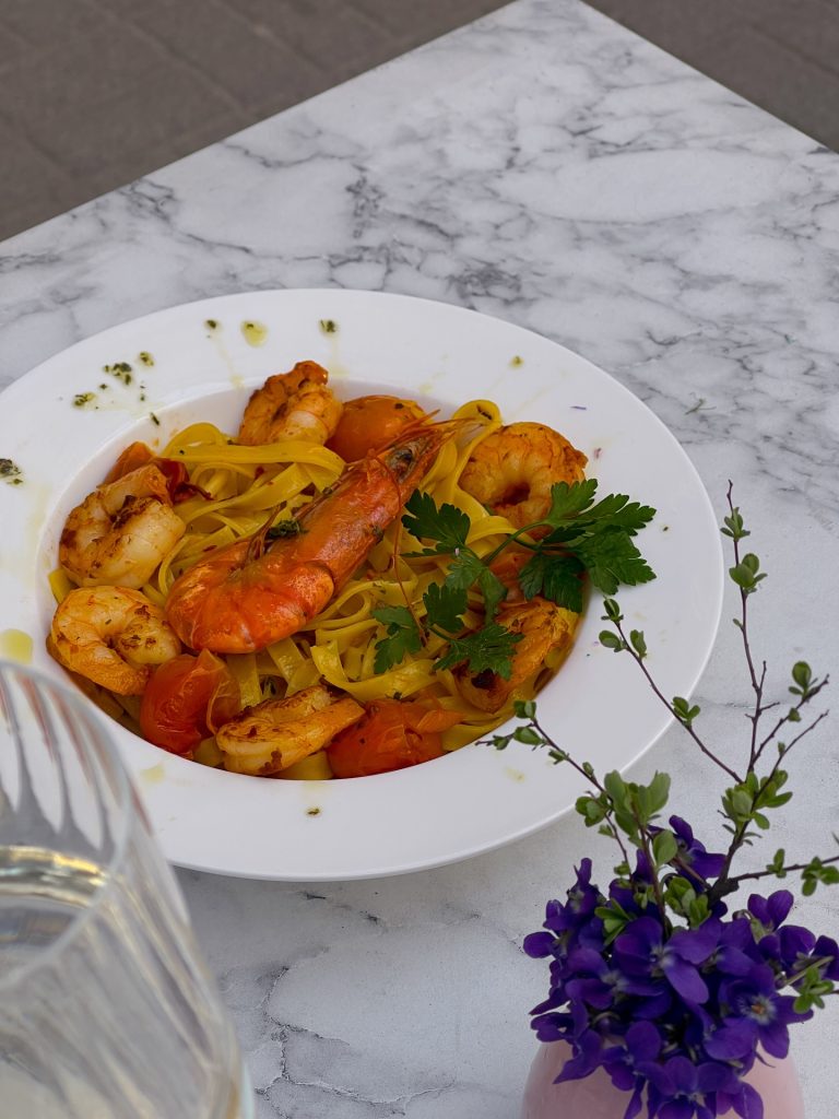 Teller mit frischer Pasta, großen Garnelen und Kirschtomaten, serviert im Freien im Bube Restauracja i Pizza in Breslau